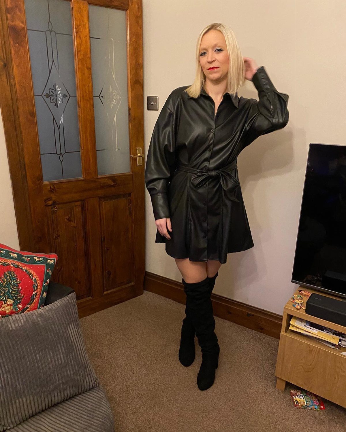 Blonde woman wearing a black leather shirt dress and black over-the-knee boots.