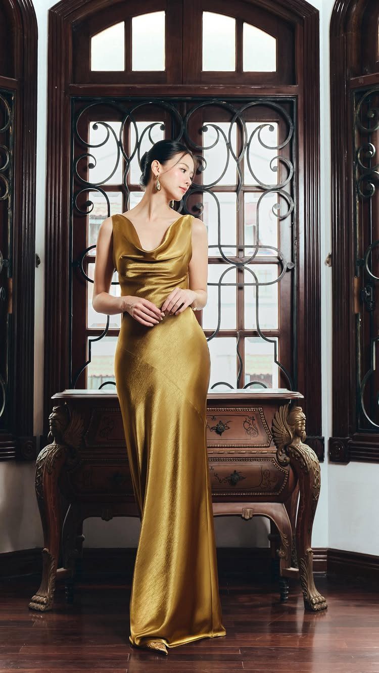 Woman in a long metallic gold satin gown standing in a classic room.