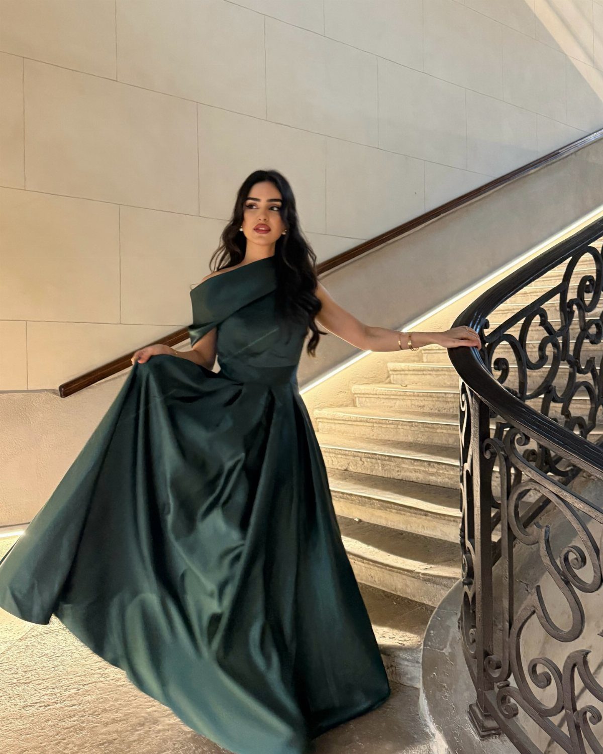 Woman in an emerald green satin gown posing on a stone staircase