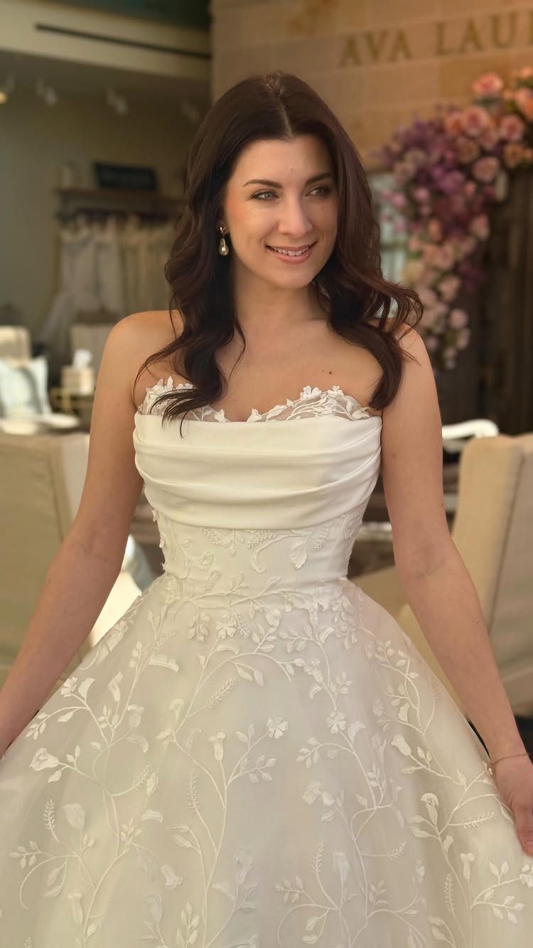 Woman wearing a white strapless wedding gown with floral lace embroidery on the skirt.
