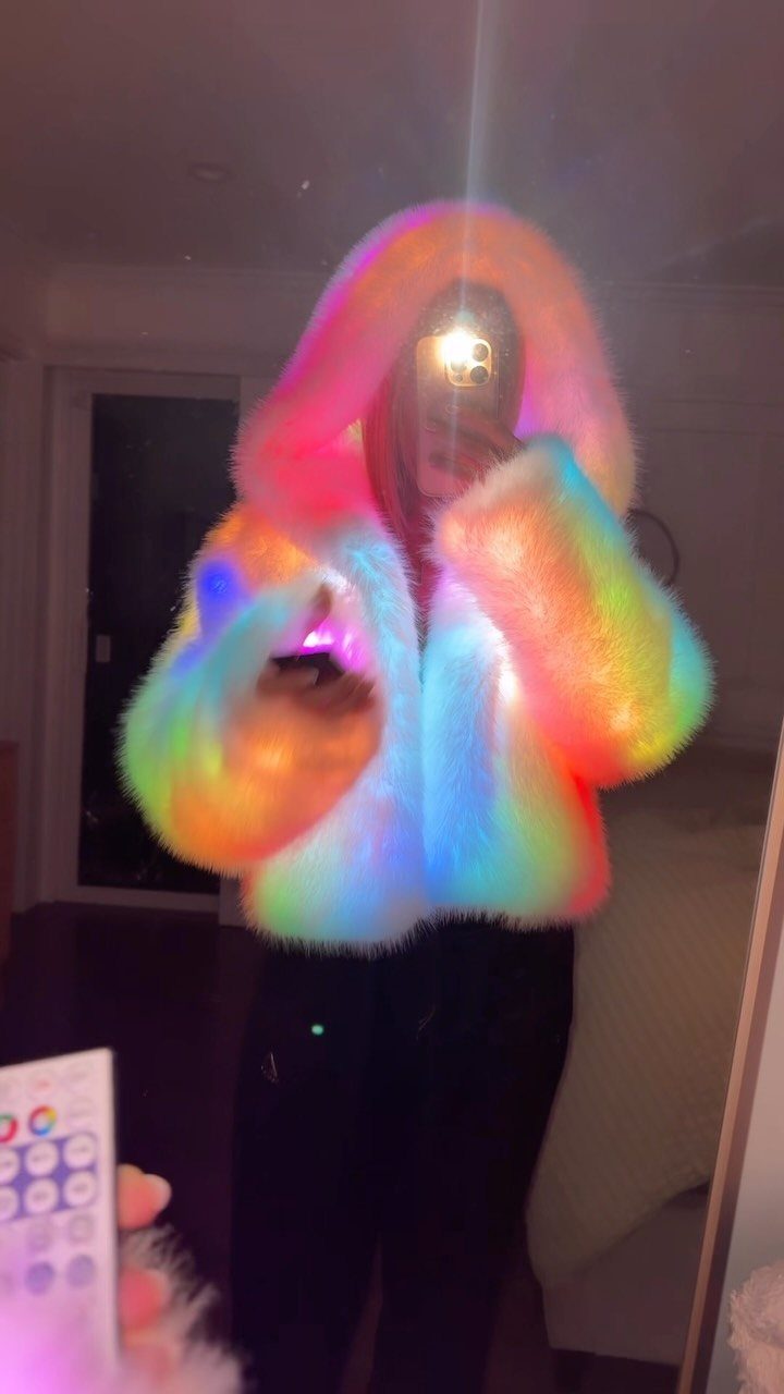 Person wearing a glowing rainbow faux fur cropped jacket with a hood.