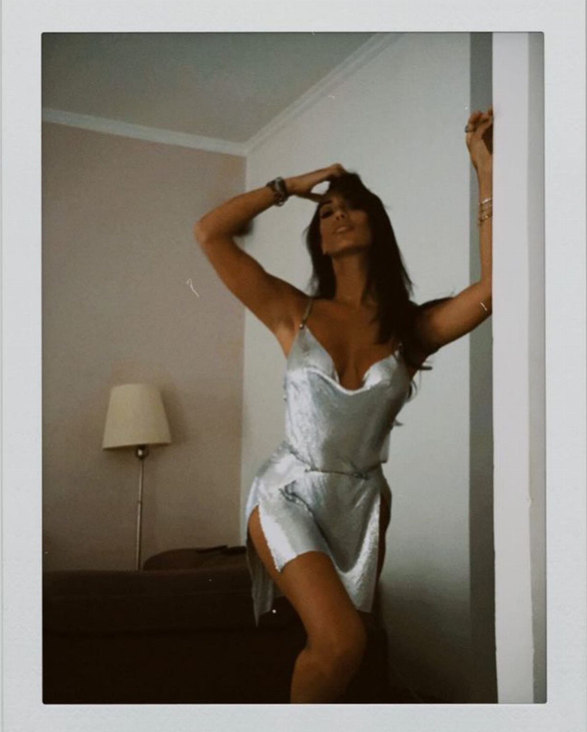 Woman posing in a shimmering silver satin mini dress in a living room
