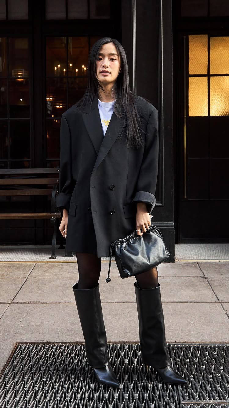 Woman wearing an oversized black blazer, black mini skirt, and tall black boots.