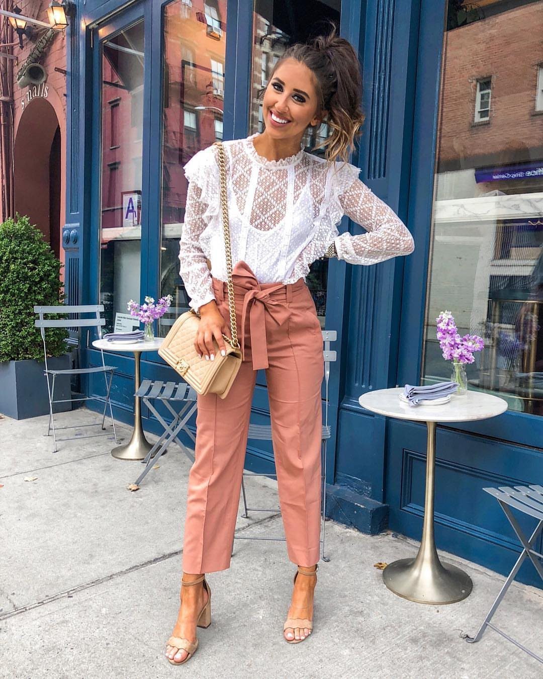 Woman wearing a white lace top and dusty rose tailored pants on a sidewalk