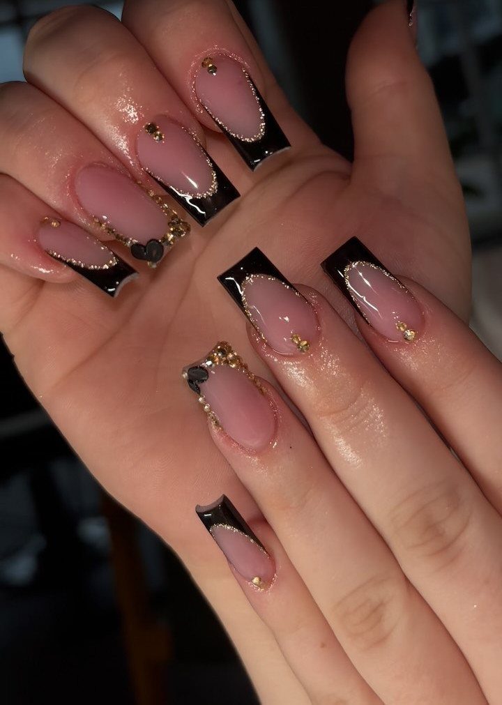 Long coffin nails with black French tips and gold glitter accents on nude base.