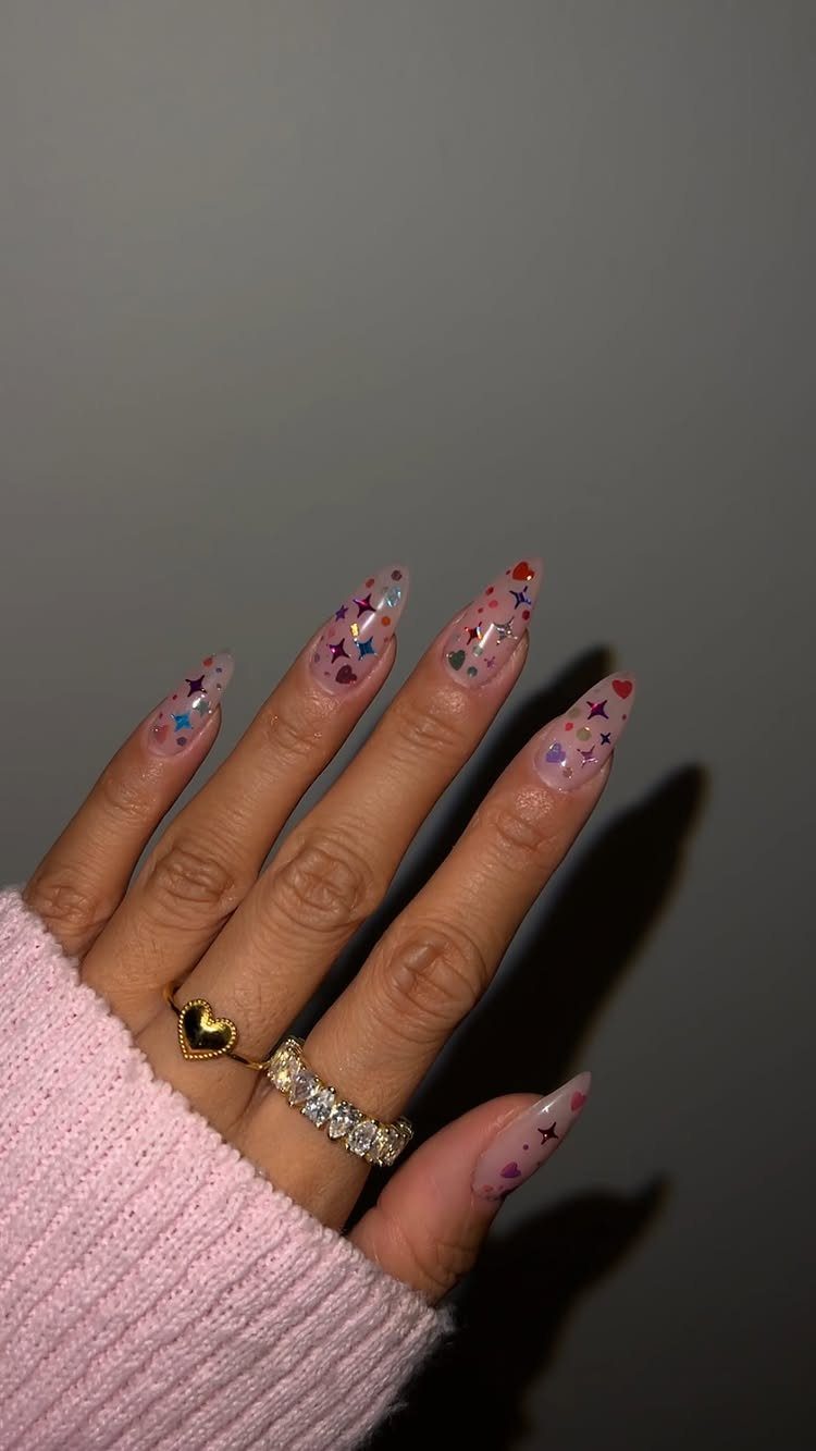 Almond nails with colorful star and heart confetti sequins and gold rings.