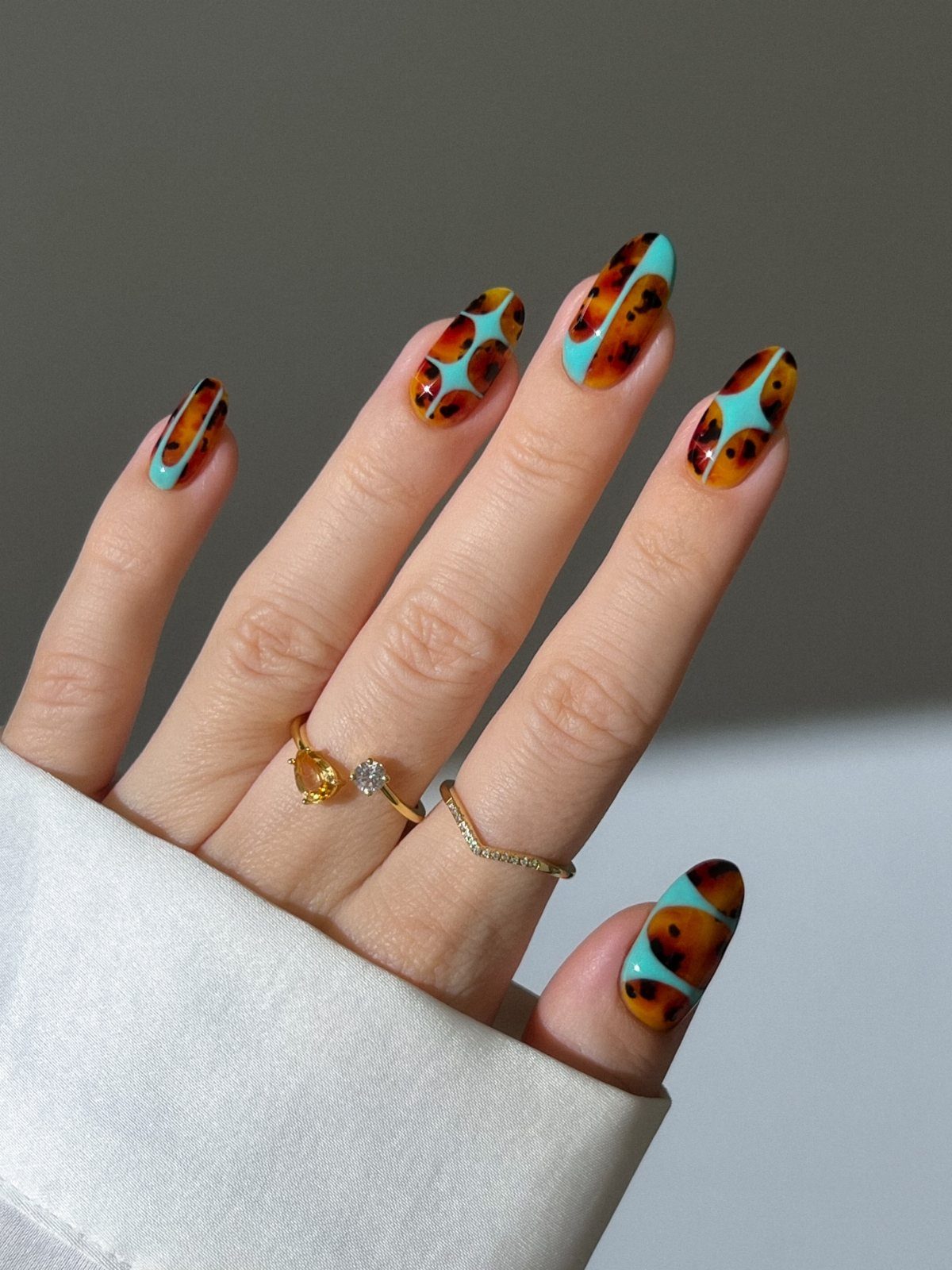 Hand with tortoiseshell and turquoise blue nail art wearing gold rings.