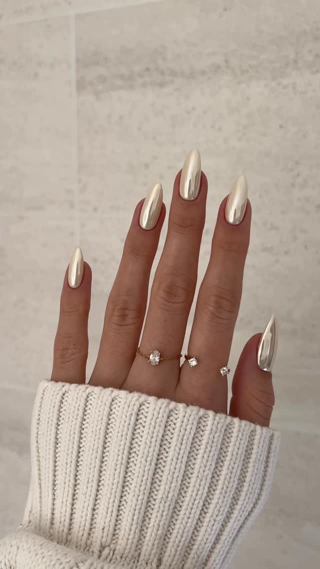 Silver chrome almond-shaped nails on a hand wearing a white ribbed sweater.