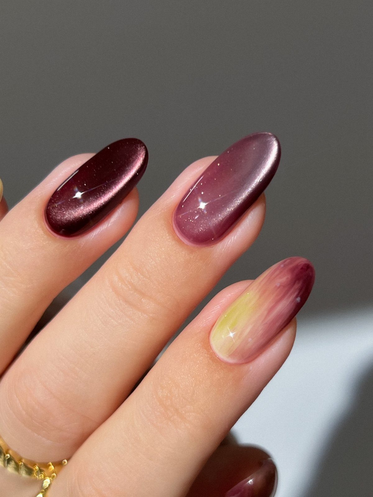 Almond-shaped nails with metallic burgundy, purple, and gradient iridescent polish.
