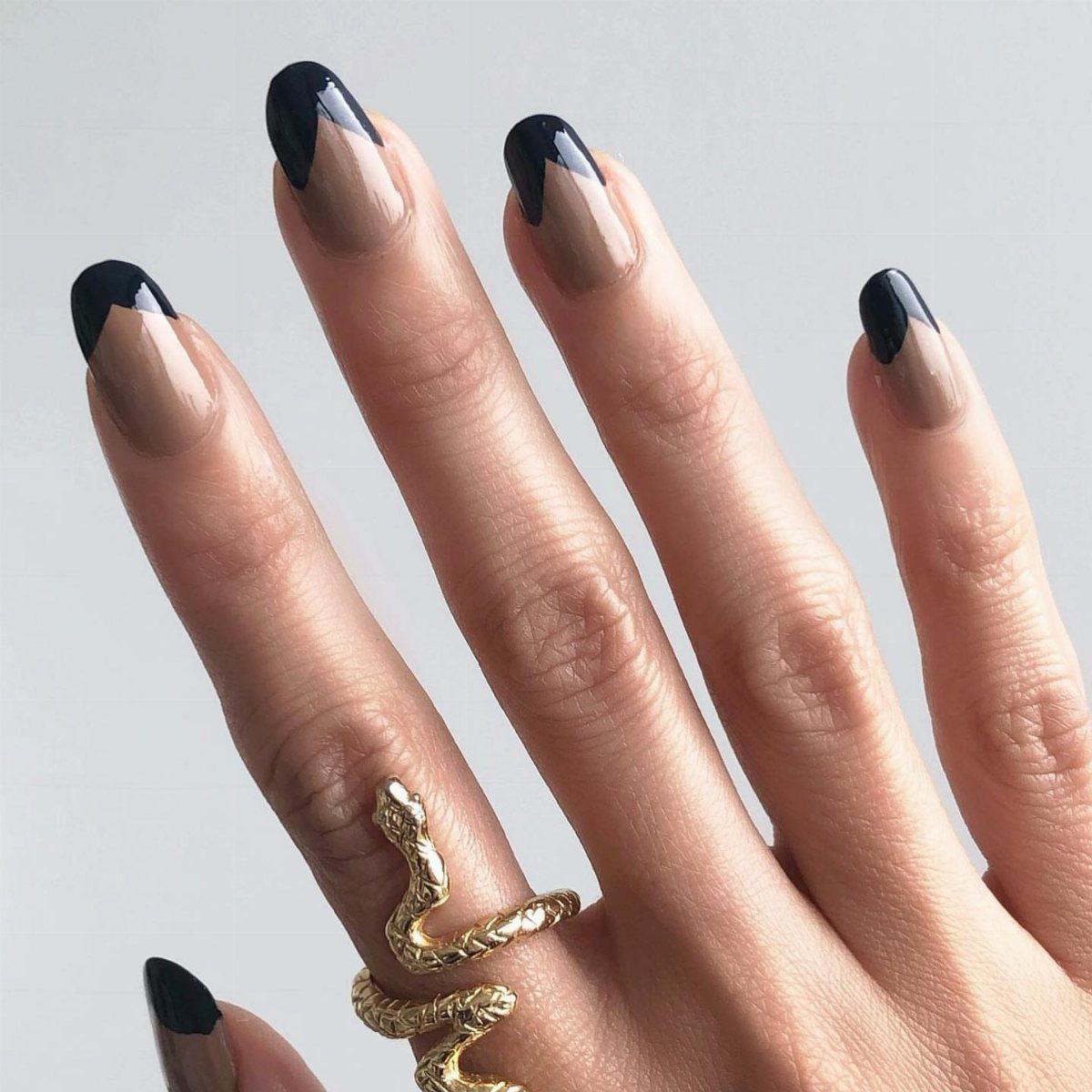 Hand with nude nails and black French tips wearing a gold snake ring.