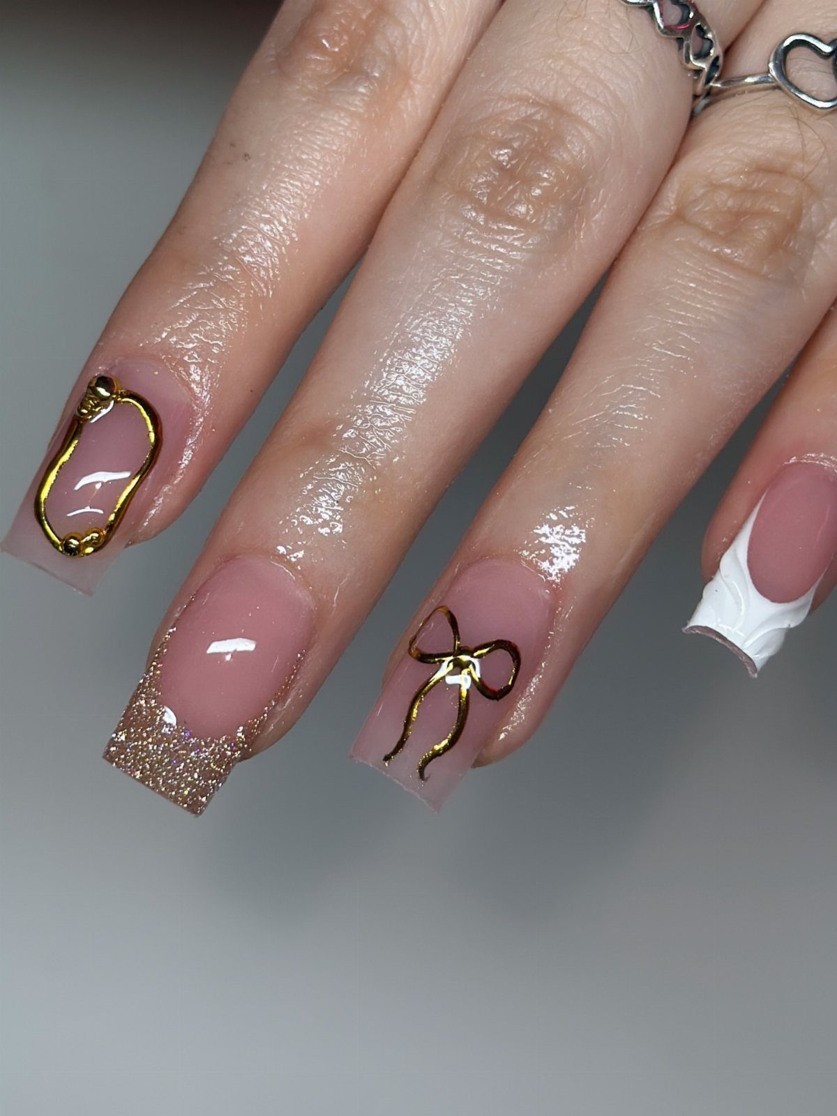 Nude manicured nails with gold glitter tips and gold bow nail art.