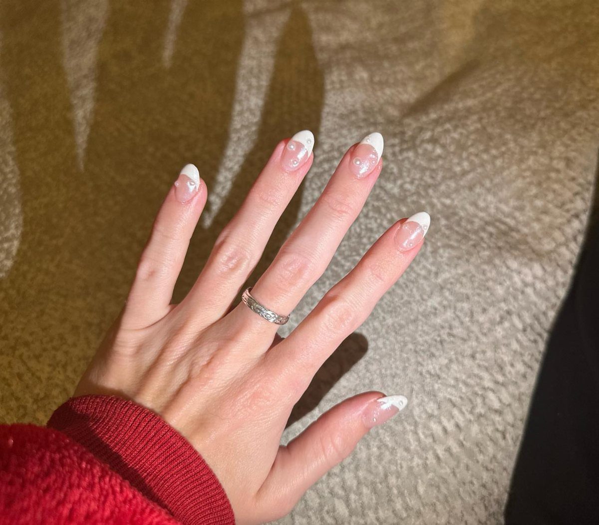 Hand with white French tip nails accented with small white pearl beads.