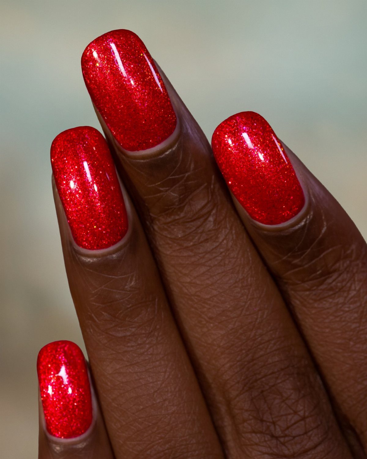 Glittery red manicure on long square nails of a dark-skinned hand.