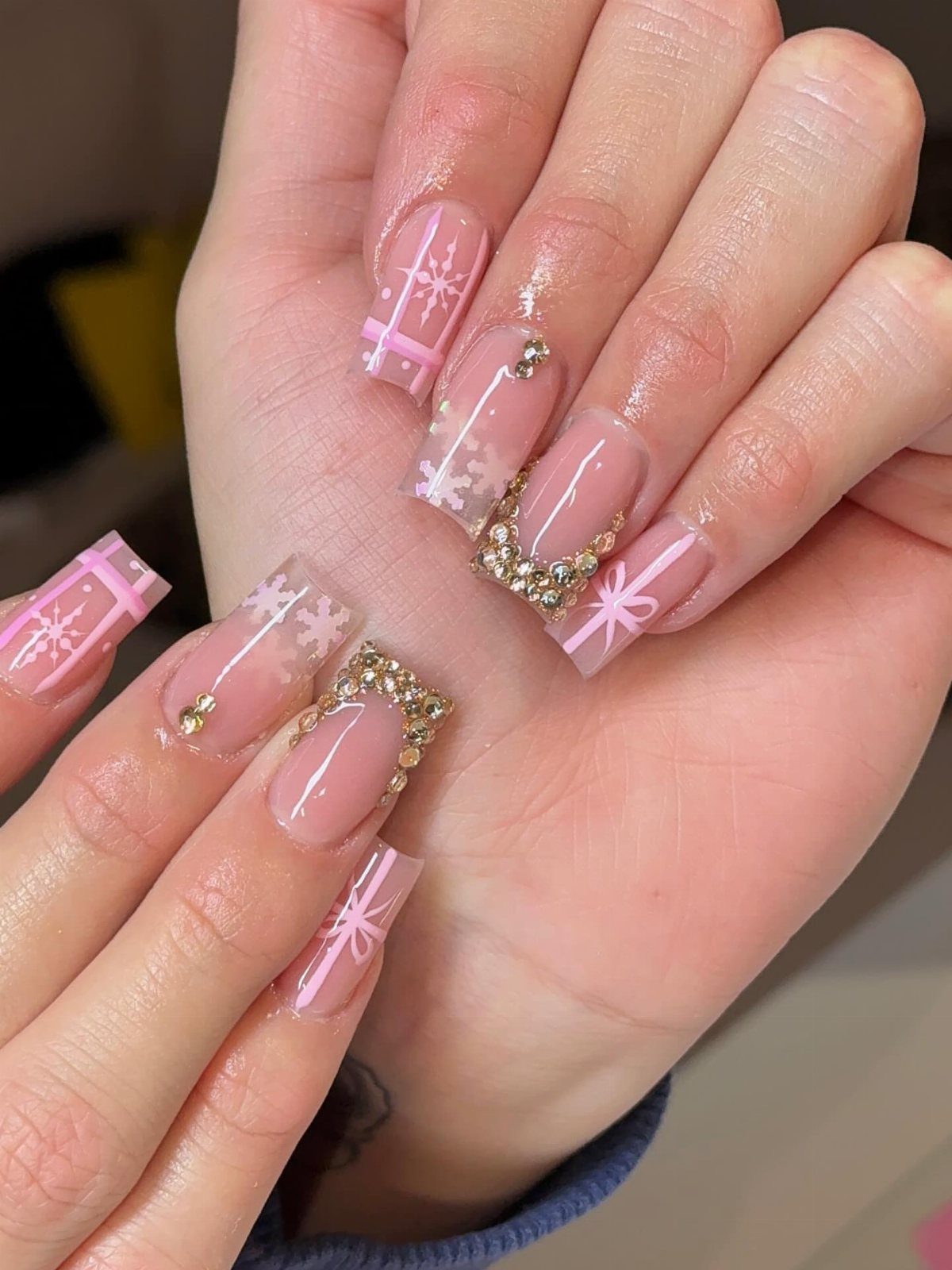 Long acrylic nails decorated with pink ribbons, white snowflakes, and gold rhinestones.