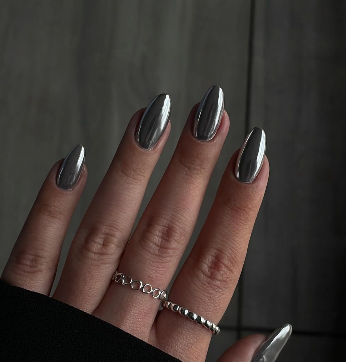 Metallic silver chrome almond-shaped nails with thin silver rings on a hand.