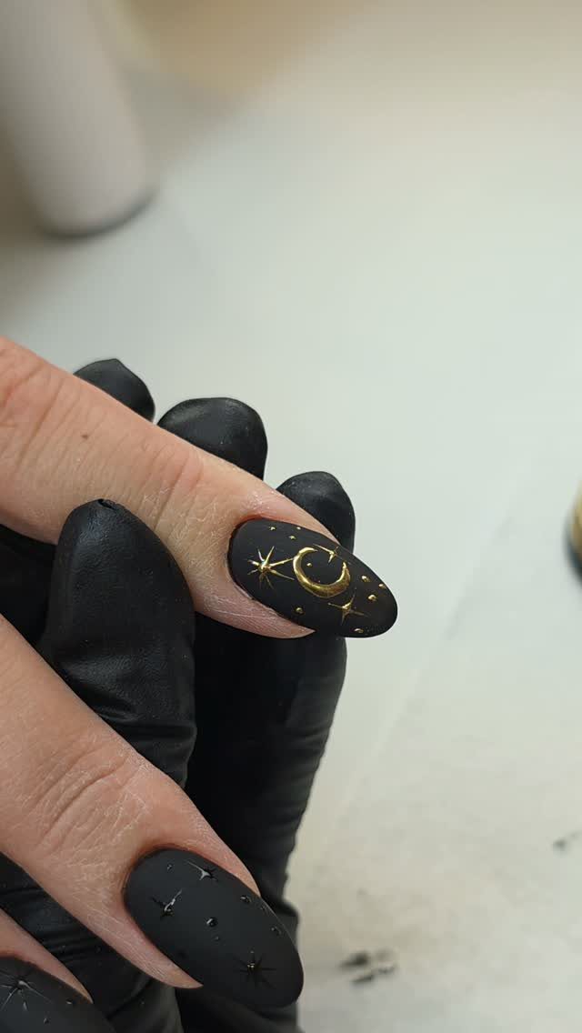Matte black nails featuring gold painted stars and a crescent moon design.