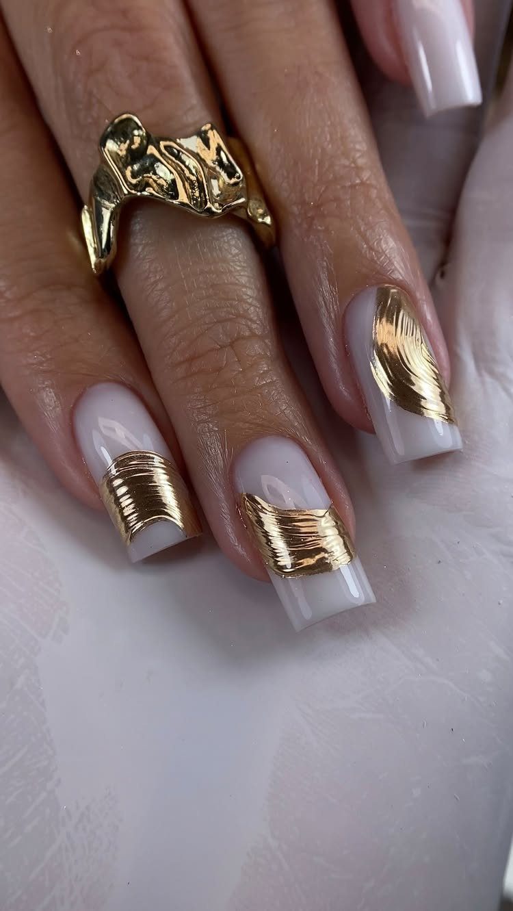 Manicured nails with milky white polish and raised, textured gold metallic accents.