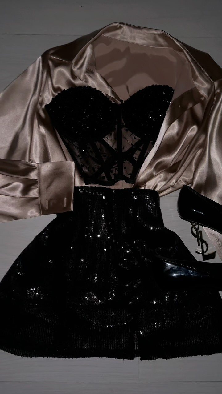 Champagne satin blazer, black lace corset, and sequined mini skirt laid out flat.