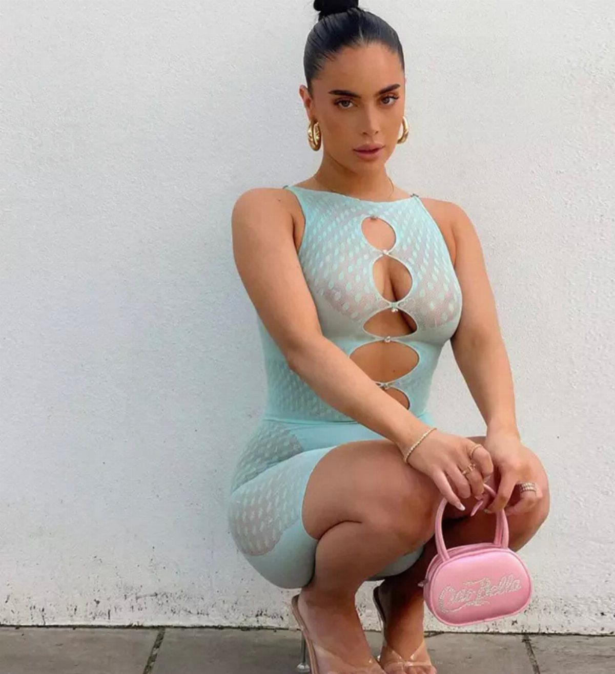 Woman in a light blue cut-out mesh dress holding a small pink handbag.