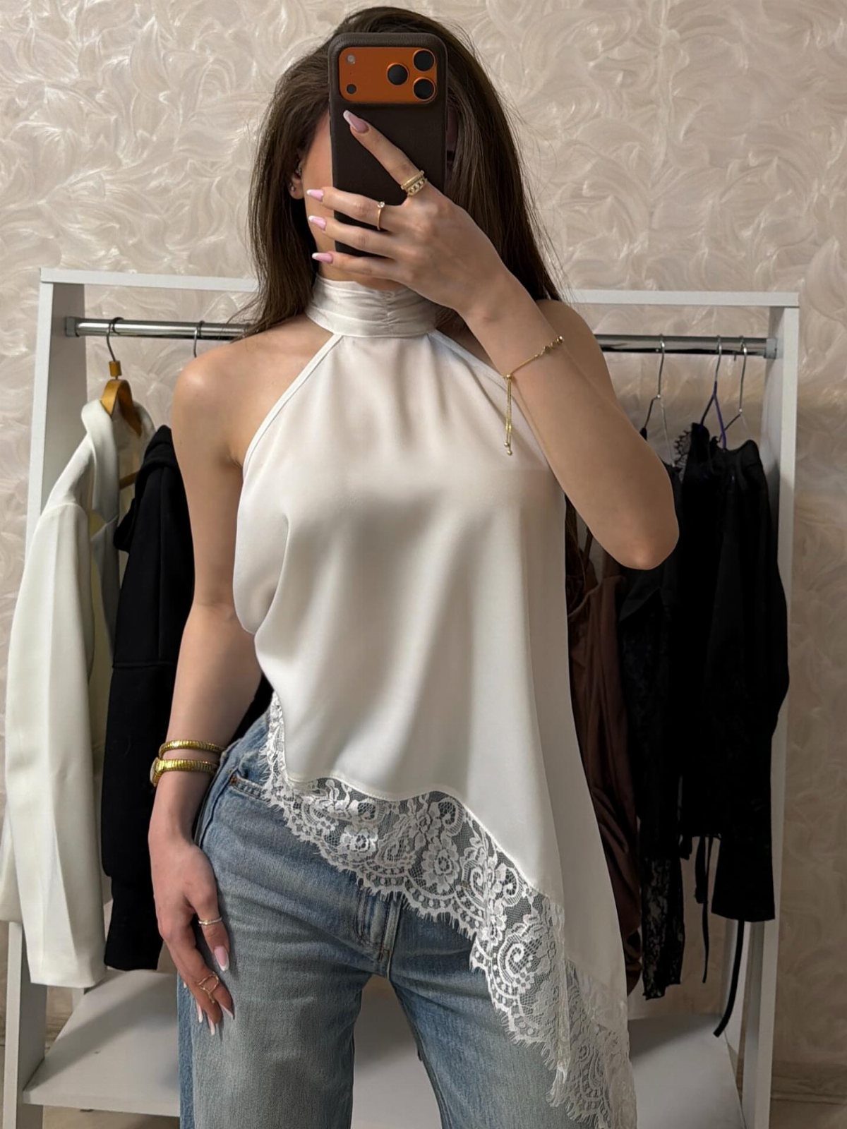 Woman wearing a white satin halter top with lace and blue jeans.