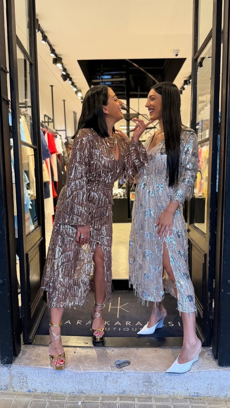 Two women wearing shimmering rose gold and silver sequin dresses in a boutique.