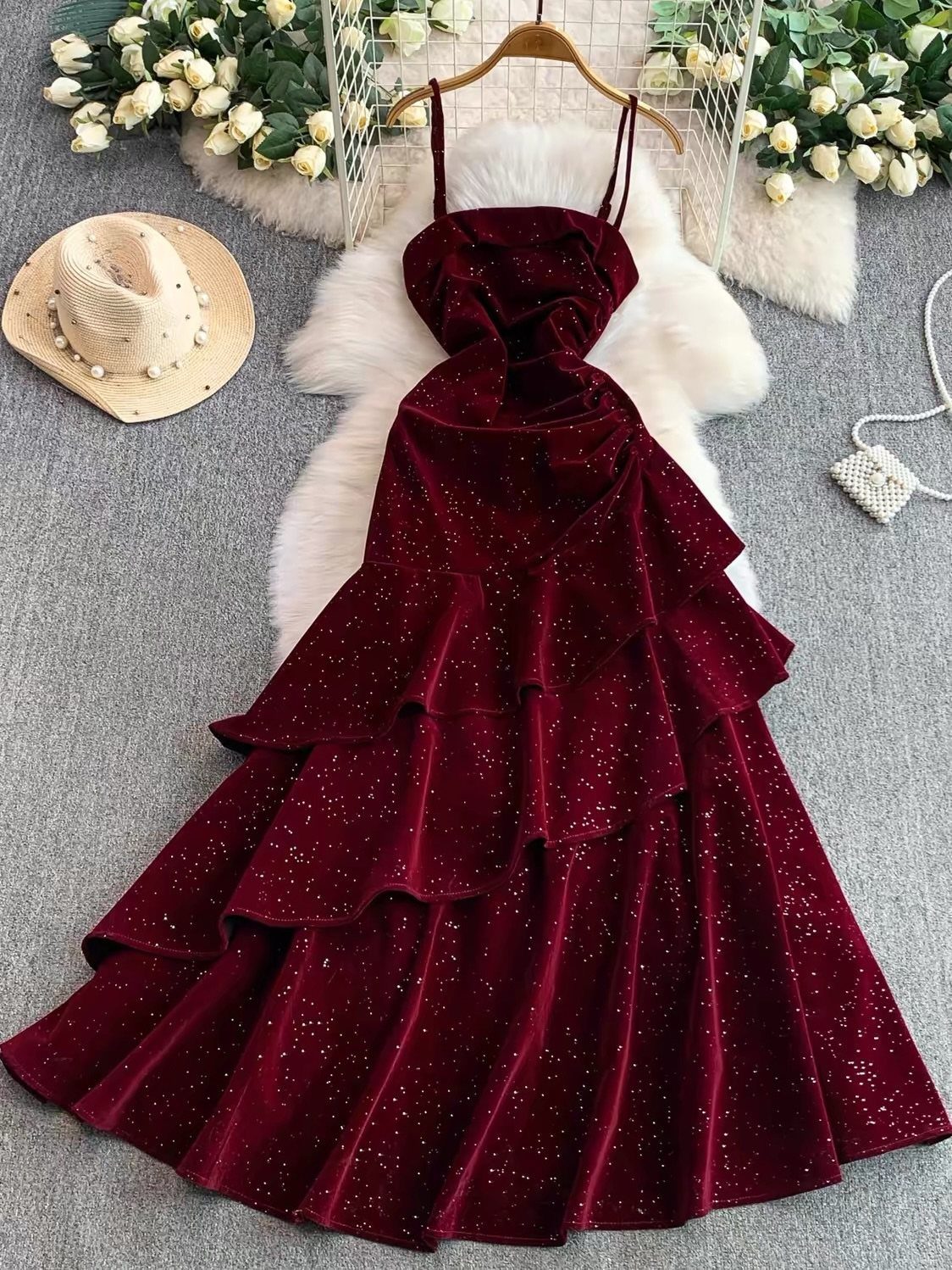 Burgundy velvet tiered maxi dress with glitter accents hanging over white faux fur.