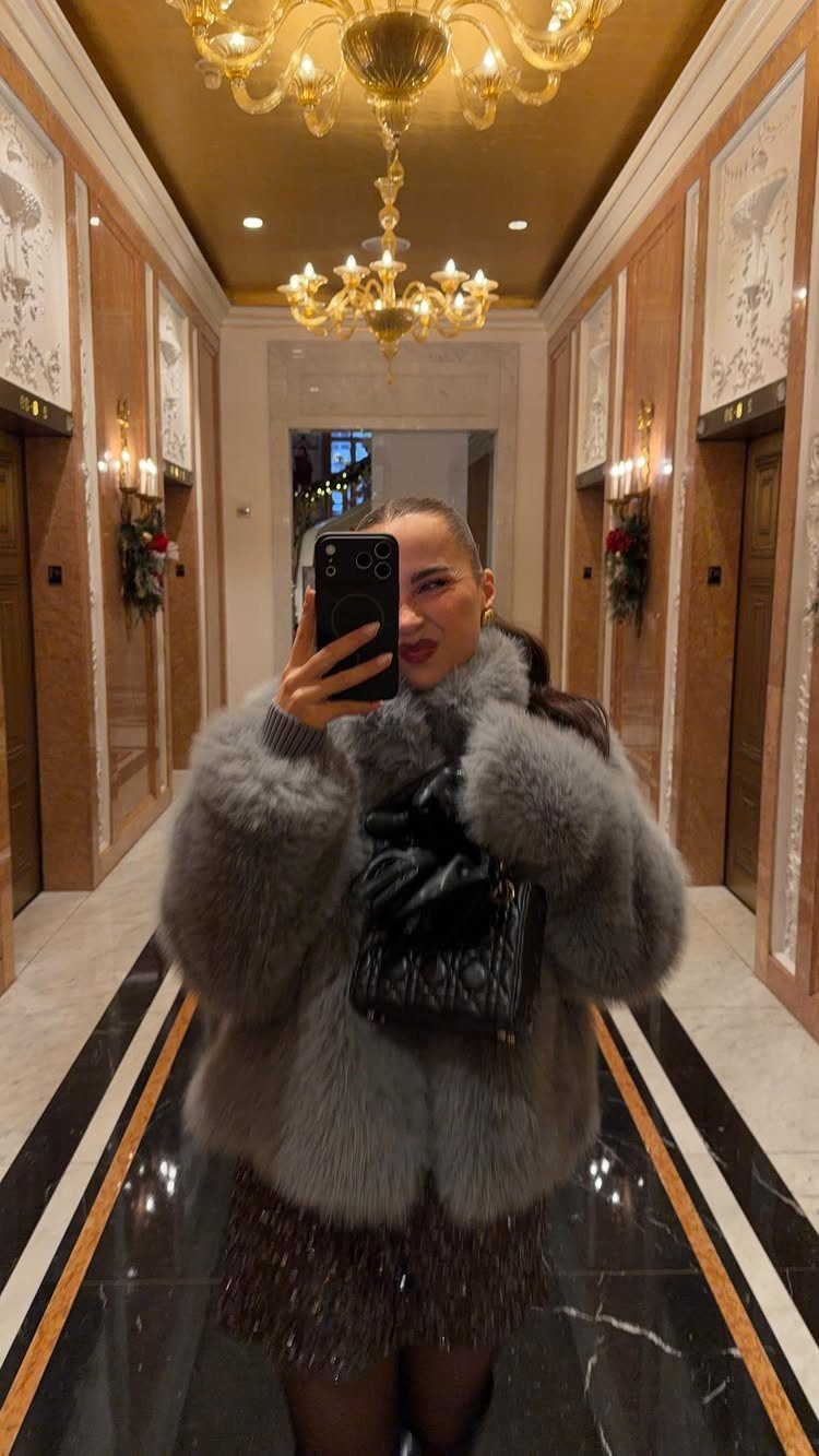Woman in a grey fur coat and sparkly skirt posing in a luxury hallway