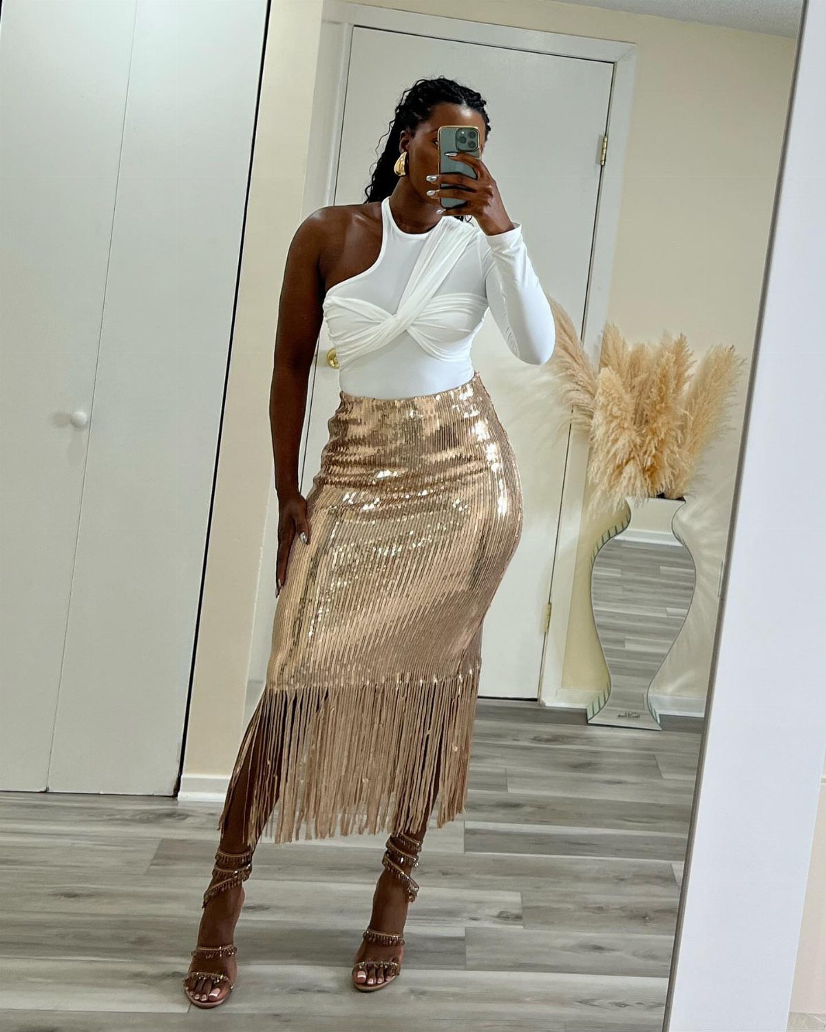 Woman wearing a white one-shoulder top and a gold sequin fringed skirt.