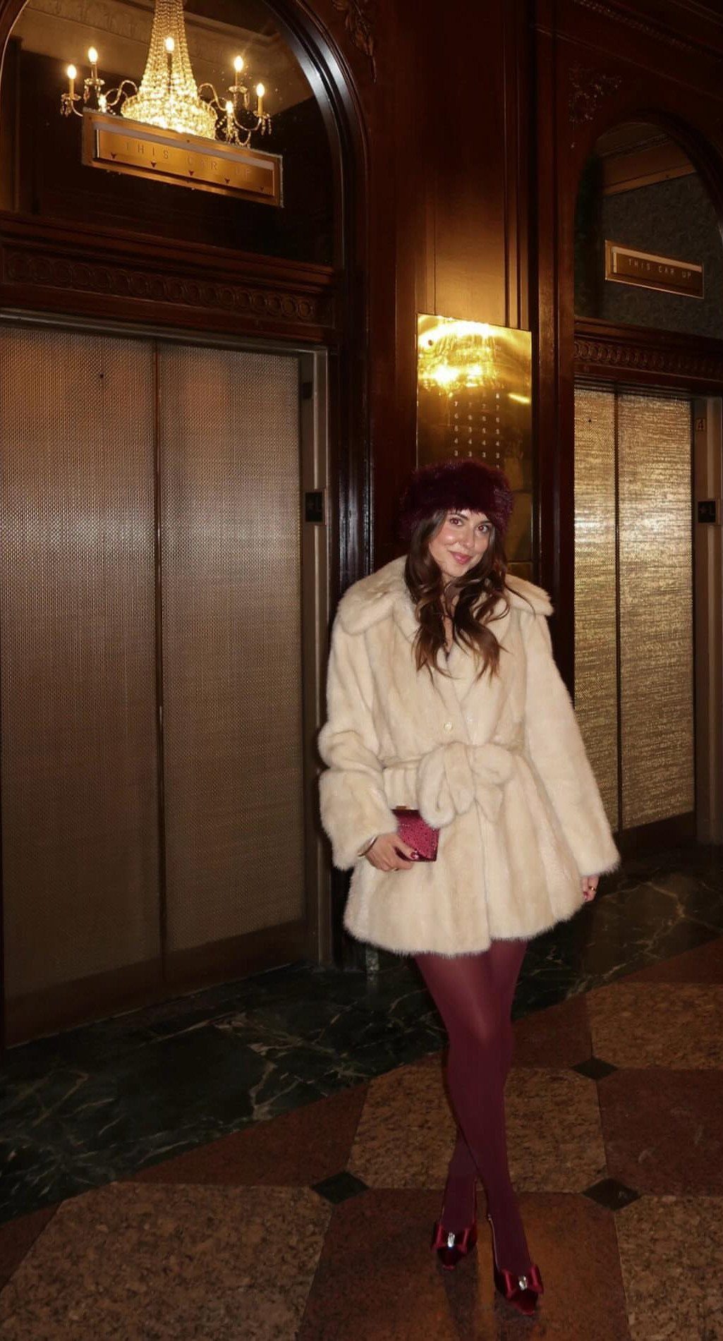 Woman in a cream faux fur coat and burgundy accessories in a luxury lobby