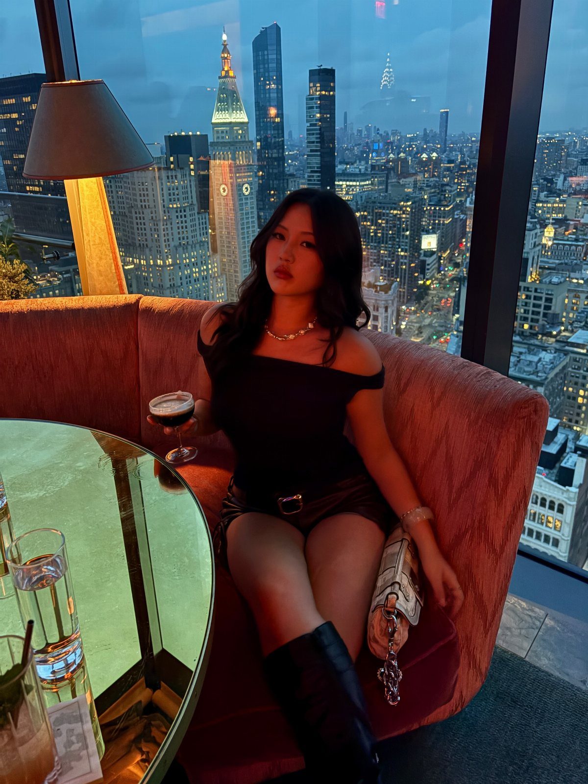 Woman in black outfit sitting in a red booth overlooking New York City skyline