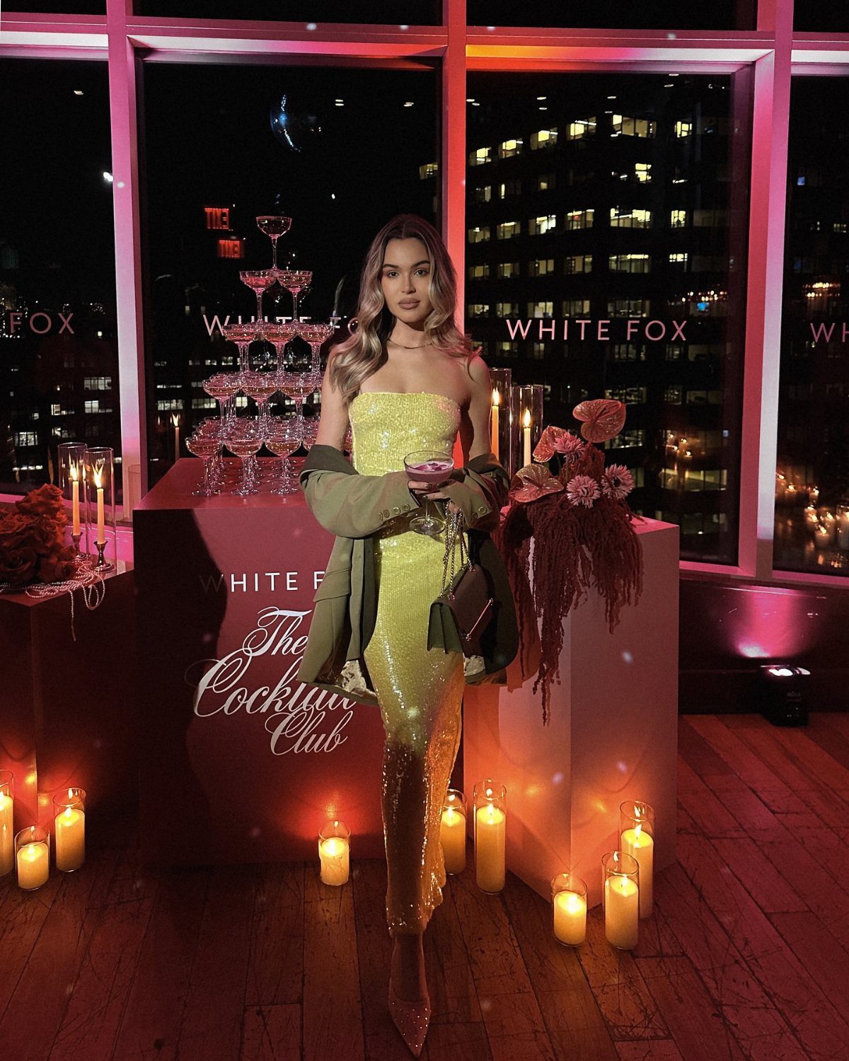 Woman in a shimmering gold dress and green jacket posing at a party.