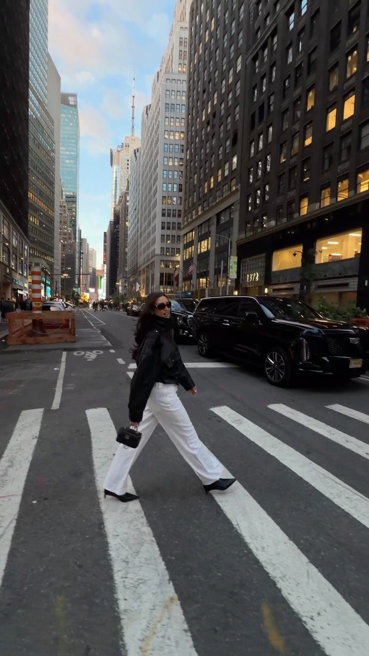 Woman in black leather jacket and white trousers crossing a New York street.
