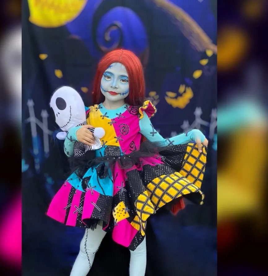 Child in a Sally patchwork costume with red hair and blue face paint.