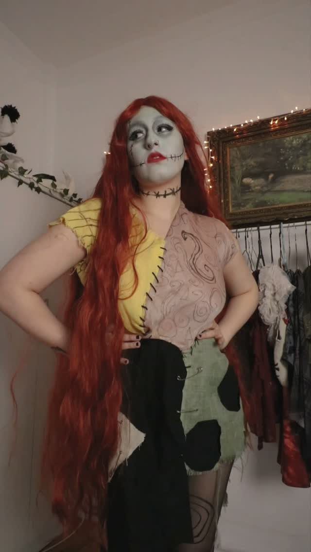 Person in a Sally costume with red hair and patchwork dress posing indoors.