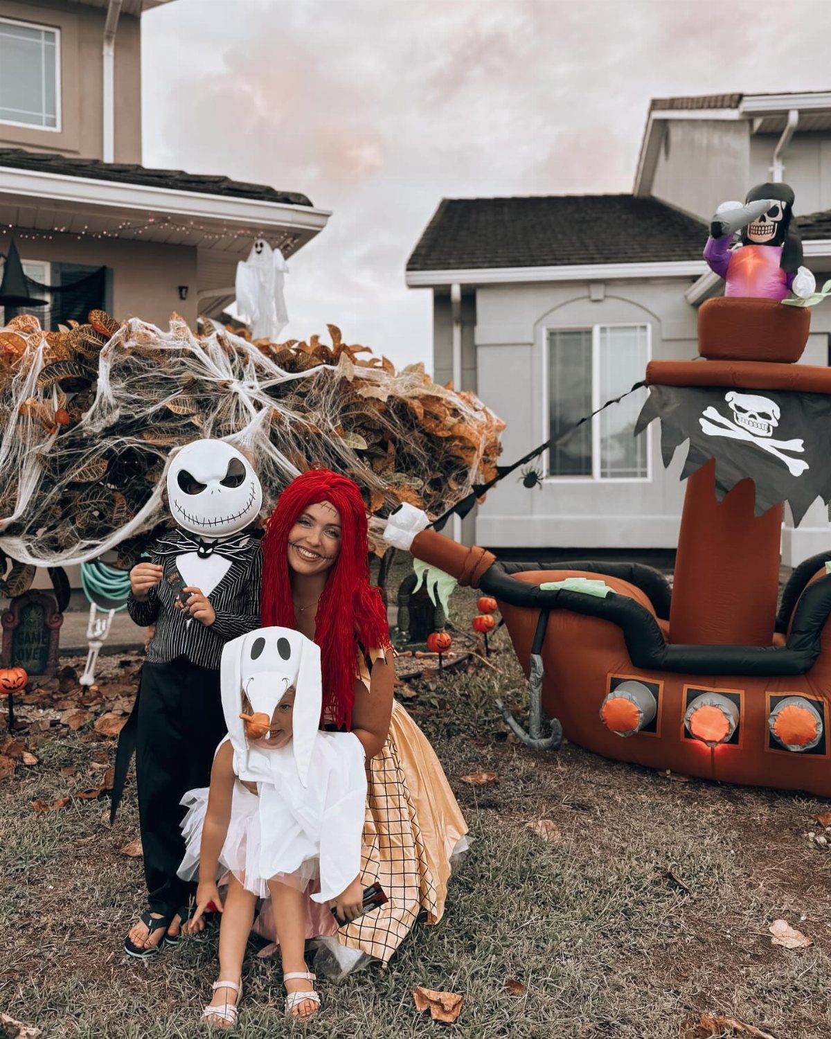 Three people in Nightmare Before Christmas costumes posing in a decorated Halloween yard.