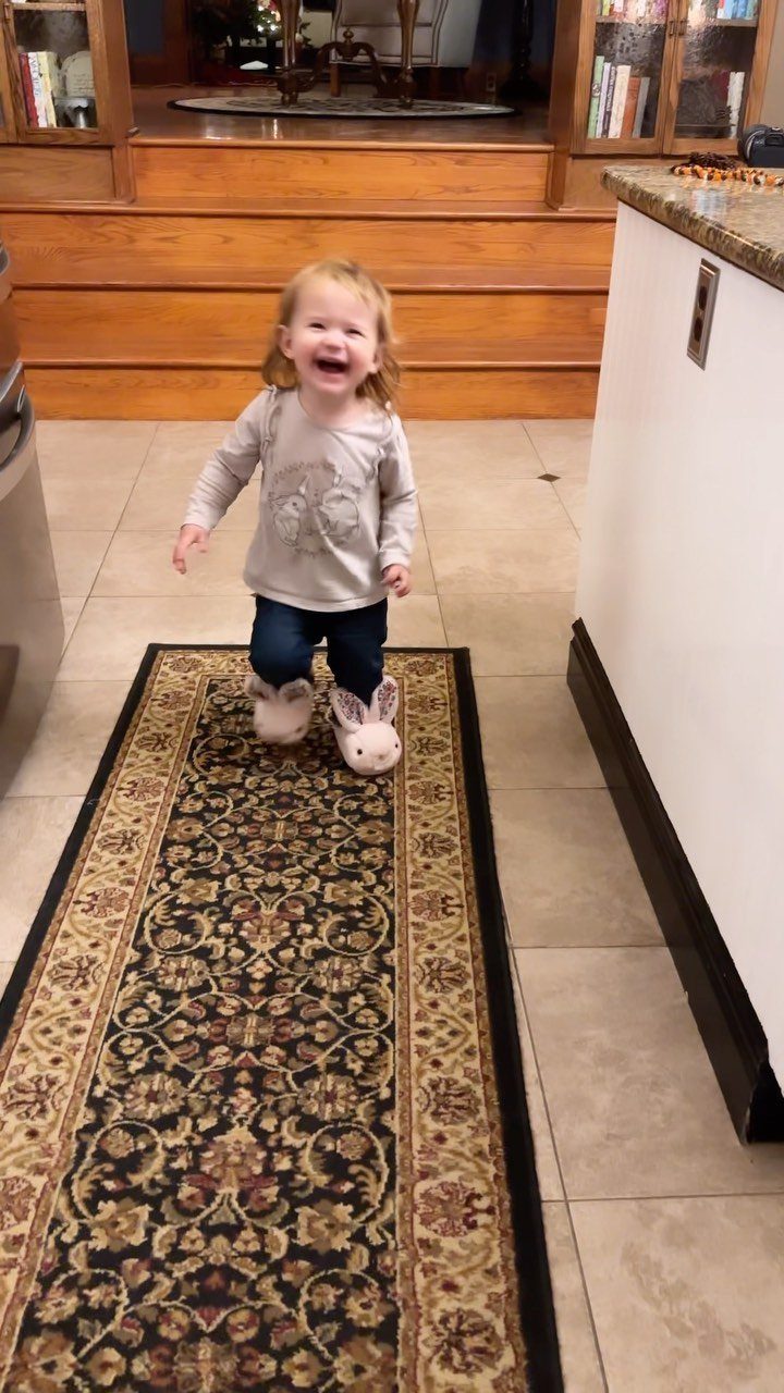Young girl smiling while wearing plush white bunny slippers on a patterned rug.