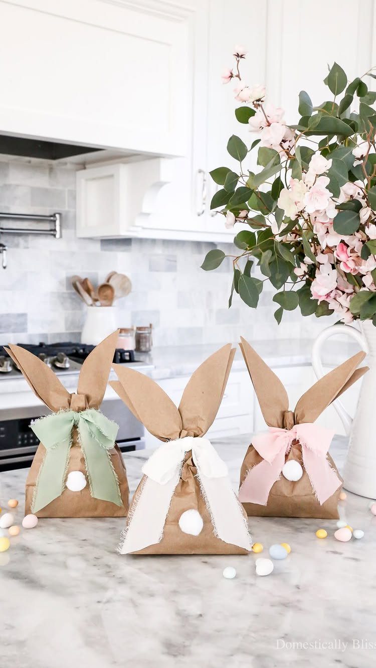 Three brown paper bunny bags with colorful ribbons on a marble kitchen counter.