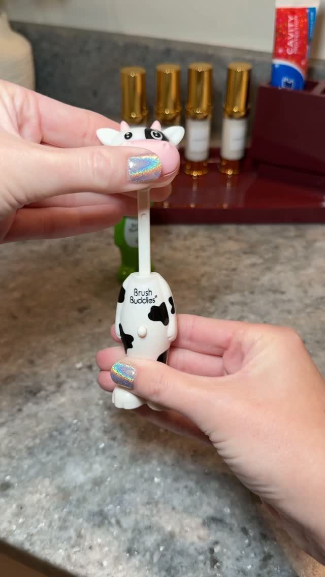Cow-themed toothbrush with animal figures on the top and bottom handle grip.