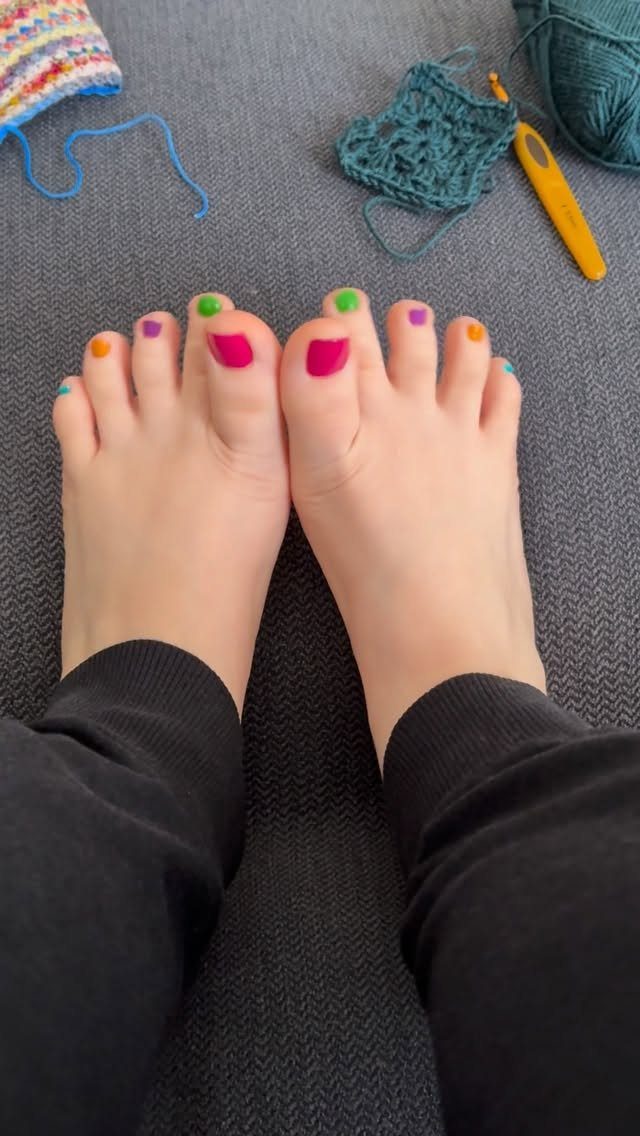 Feet with multi-colored painted toenails resting near crochet yarn and a hook.
