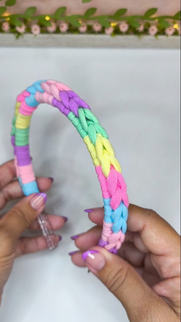 Braided colorful fabric headband held by hands with purple nail polish.