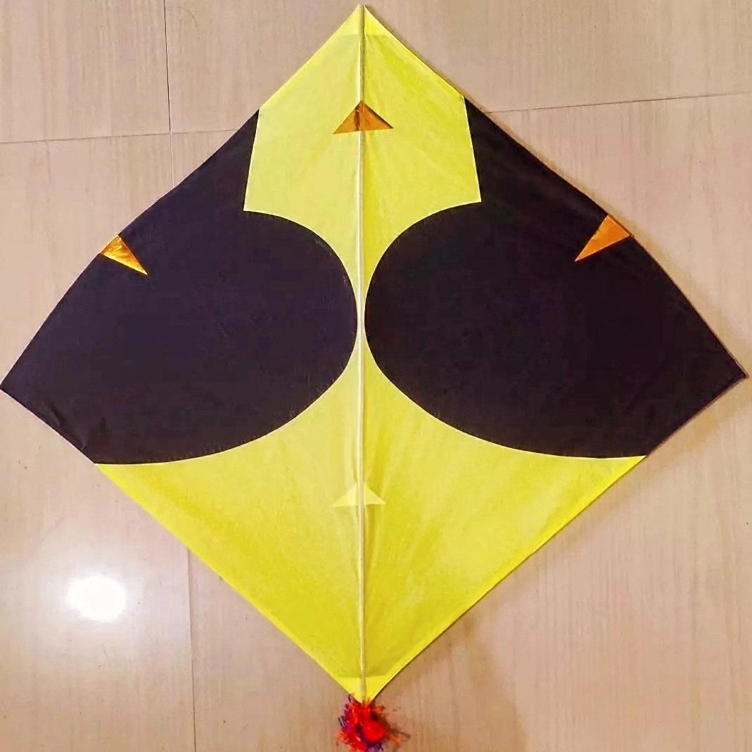 Yellow and black diamond-shaped kite lying on a light tiled floor.