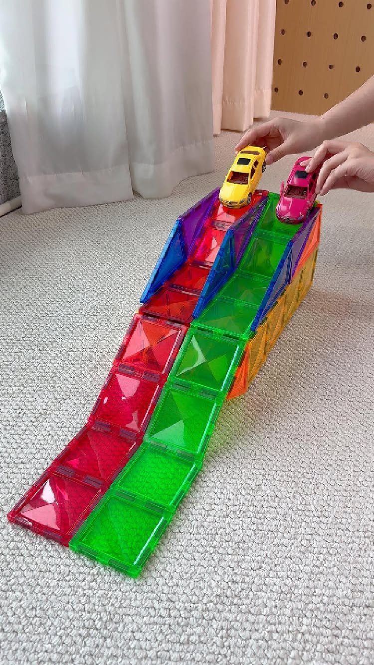 Colorful magnetic tile ramp with toy cars on a white carpeted floor.