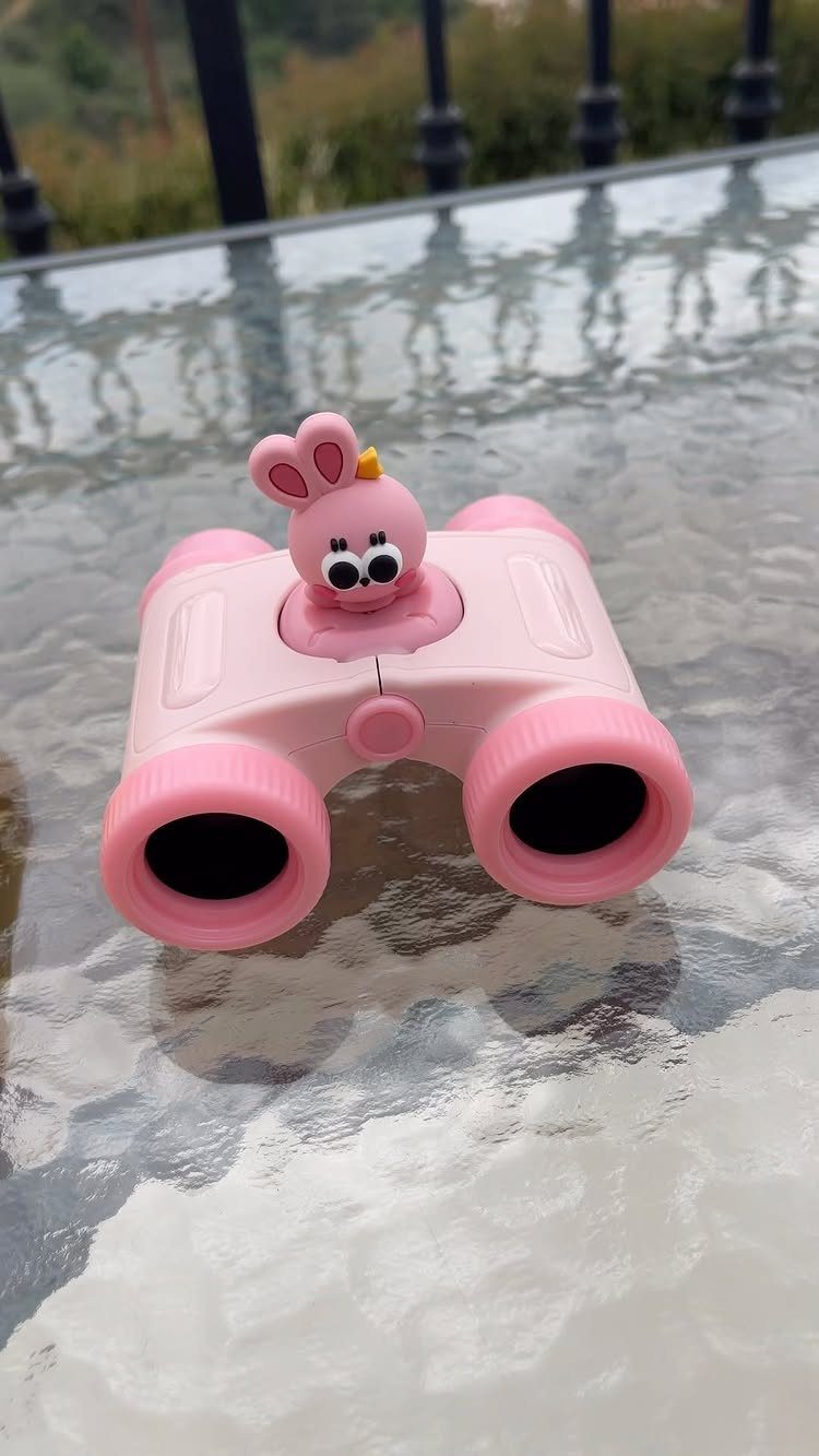Pink toy binoculars with a bunny figure on a glass table outdoors.