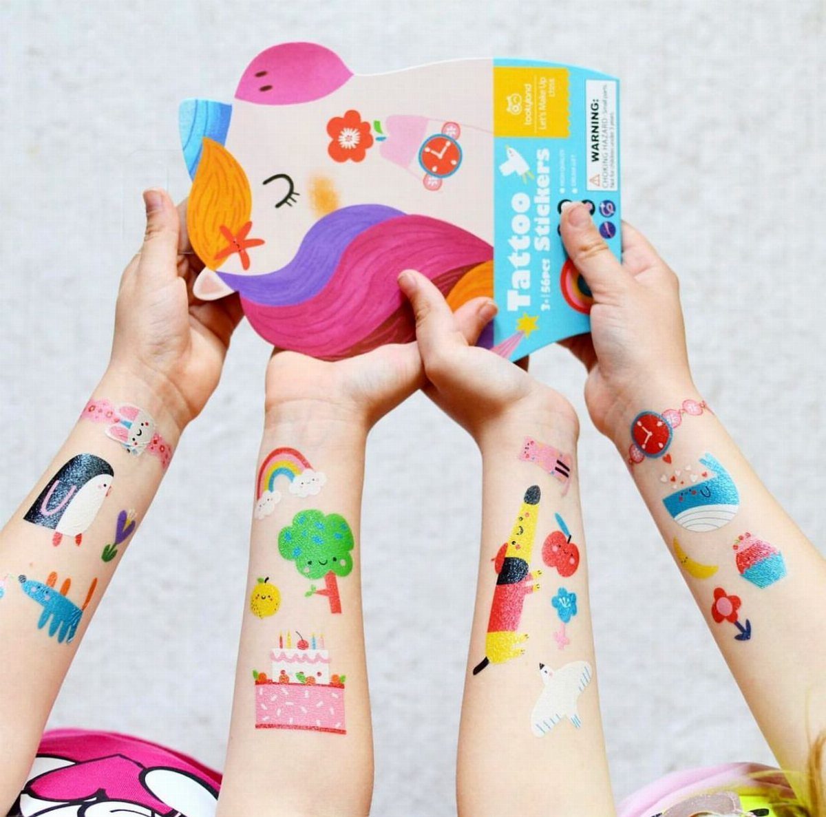 Children's arms covered in colorful temporary tattoos holding a unicorn sticker pack.