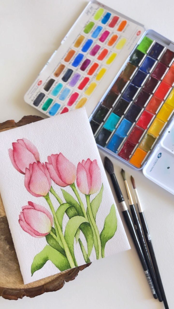 Watercolor painting of pink tulips next to a colorful paint set and brushes.