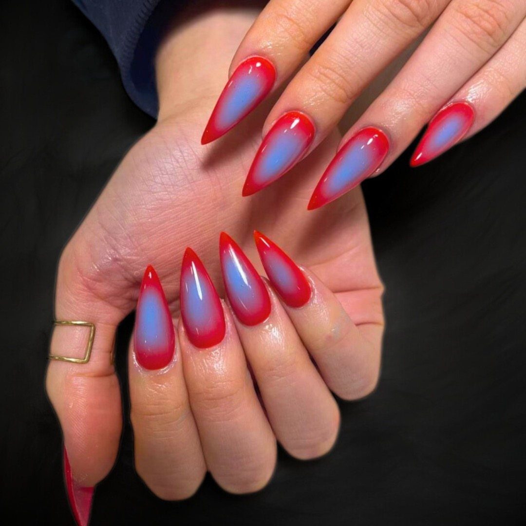 Stiletto nails with a blue to red ombre gradient on a black background