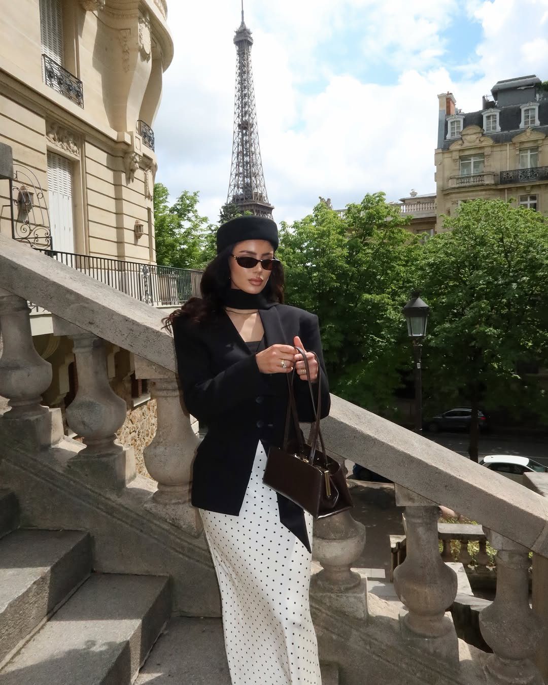 Woman in black blazer and polka-dot skirt posing with Eiffel Tower in background