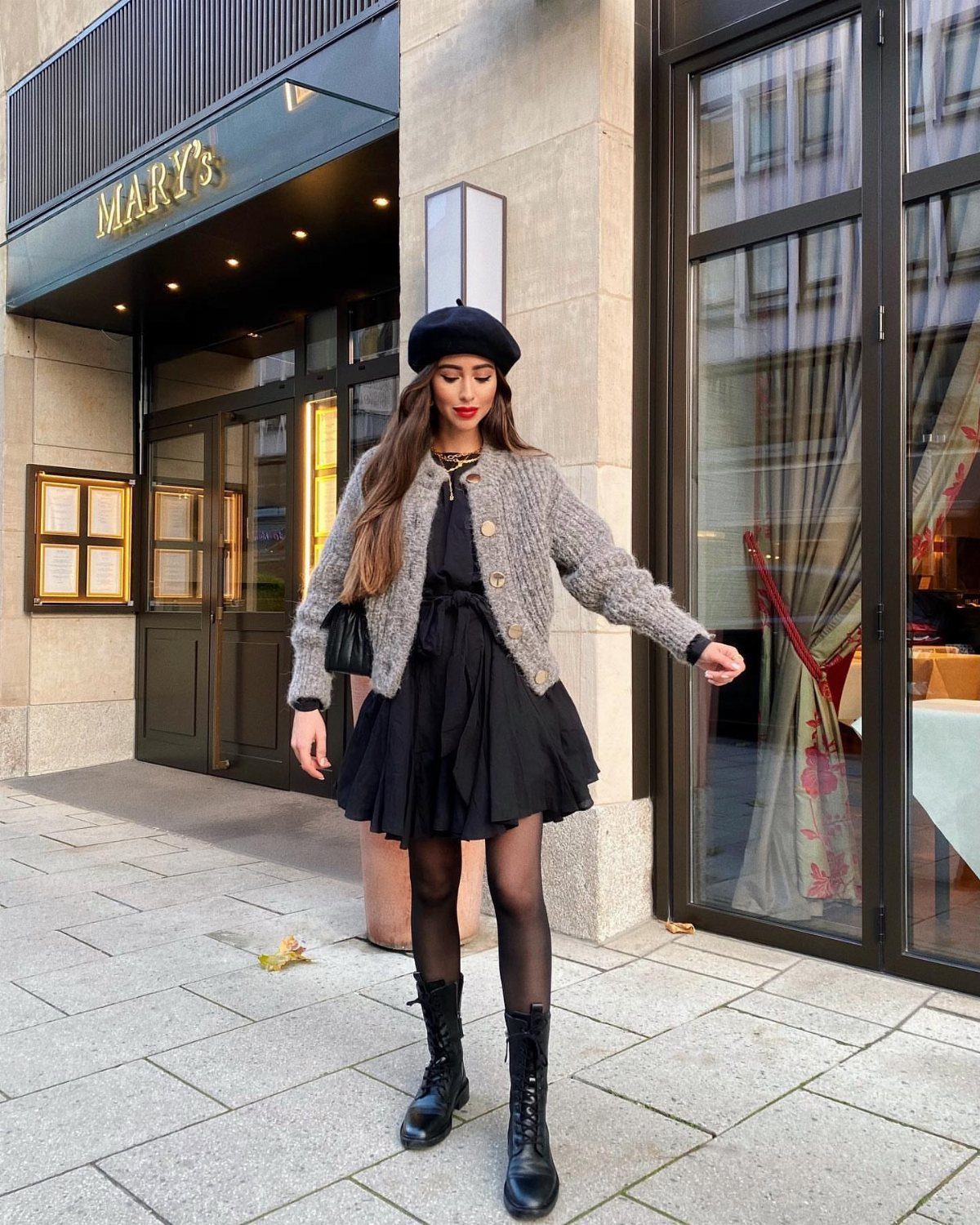 Woman in black mini dress, grey cardigan, and black beret on city street.