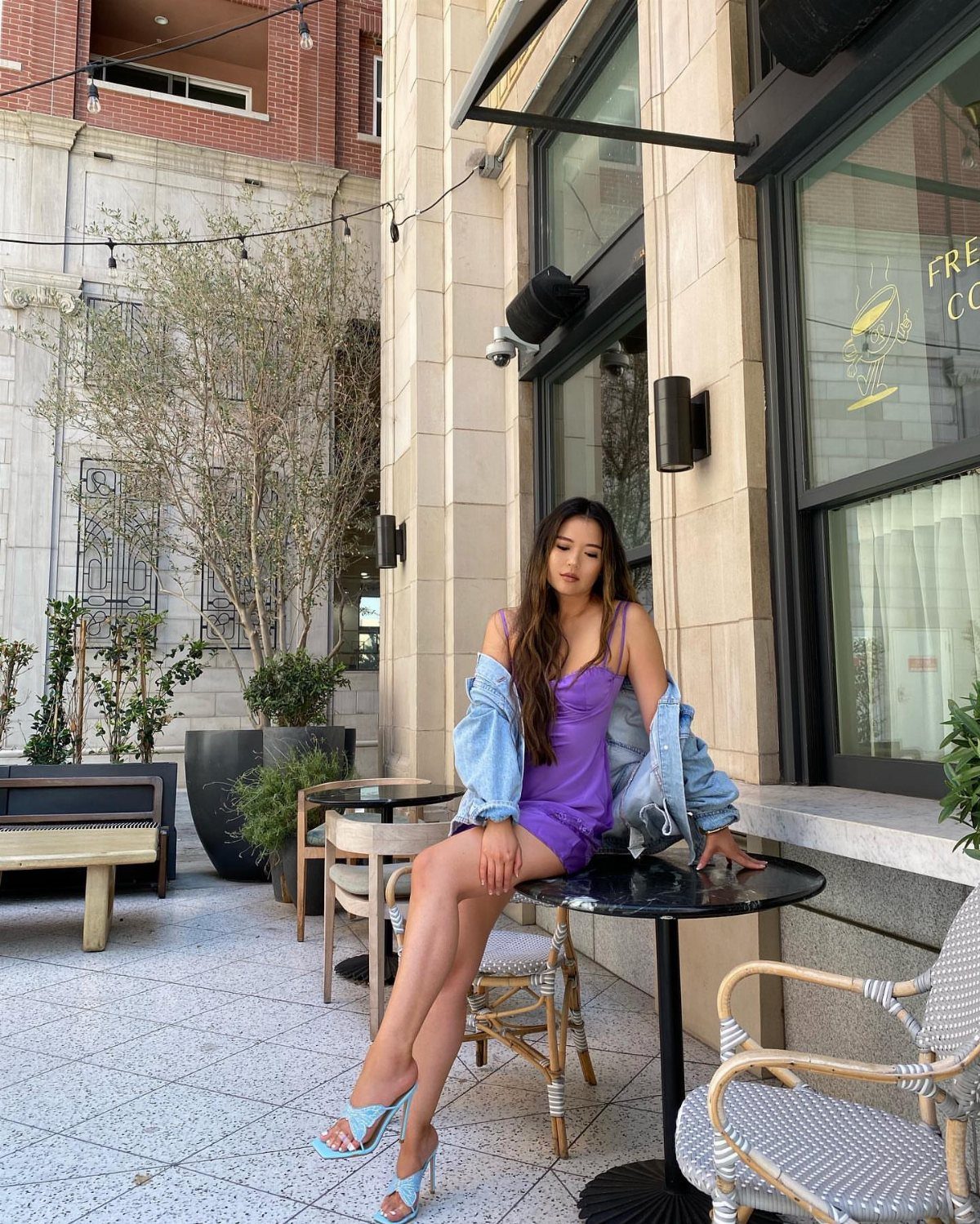 Woman in purple mini dress and blue heels sitting at outdoor cafe table