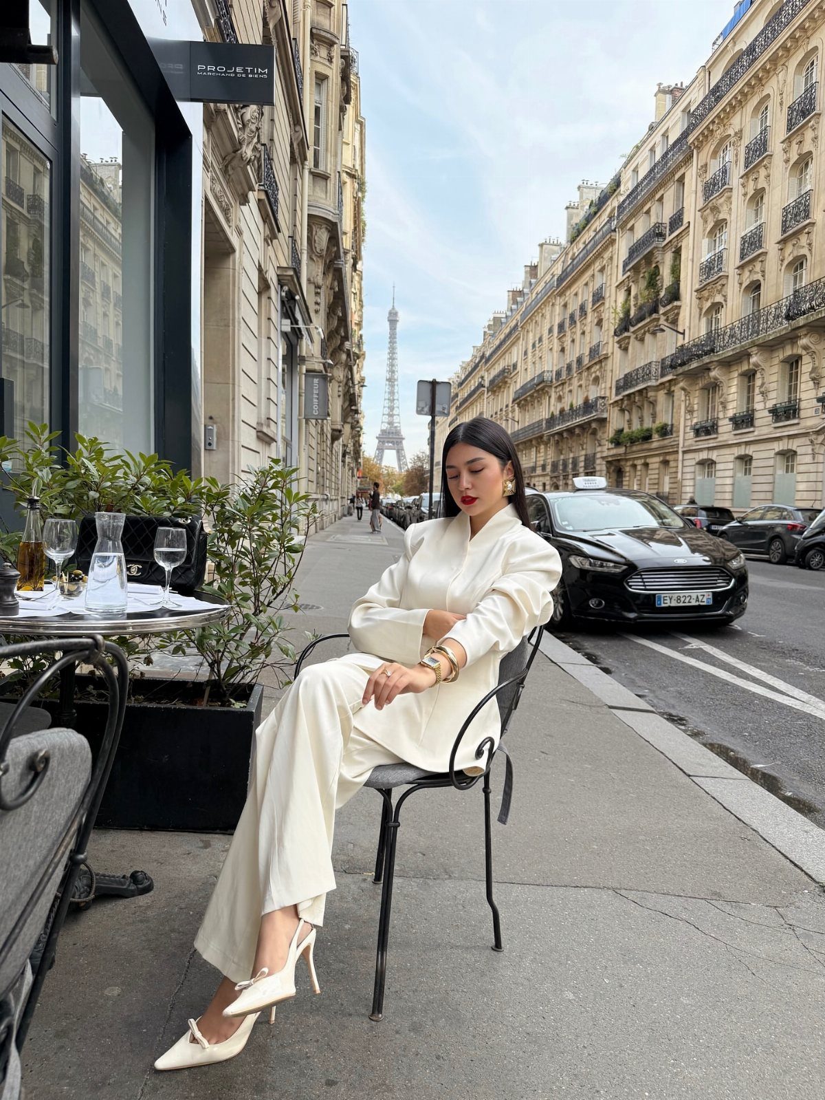 Woman in cream tailored suit sitting at a cafe with Eiffel Tower background